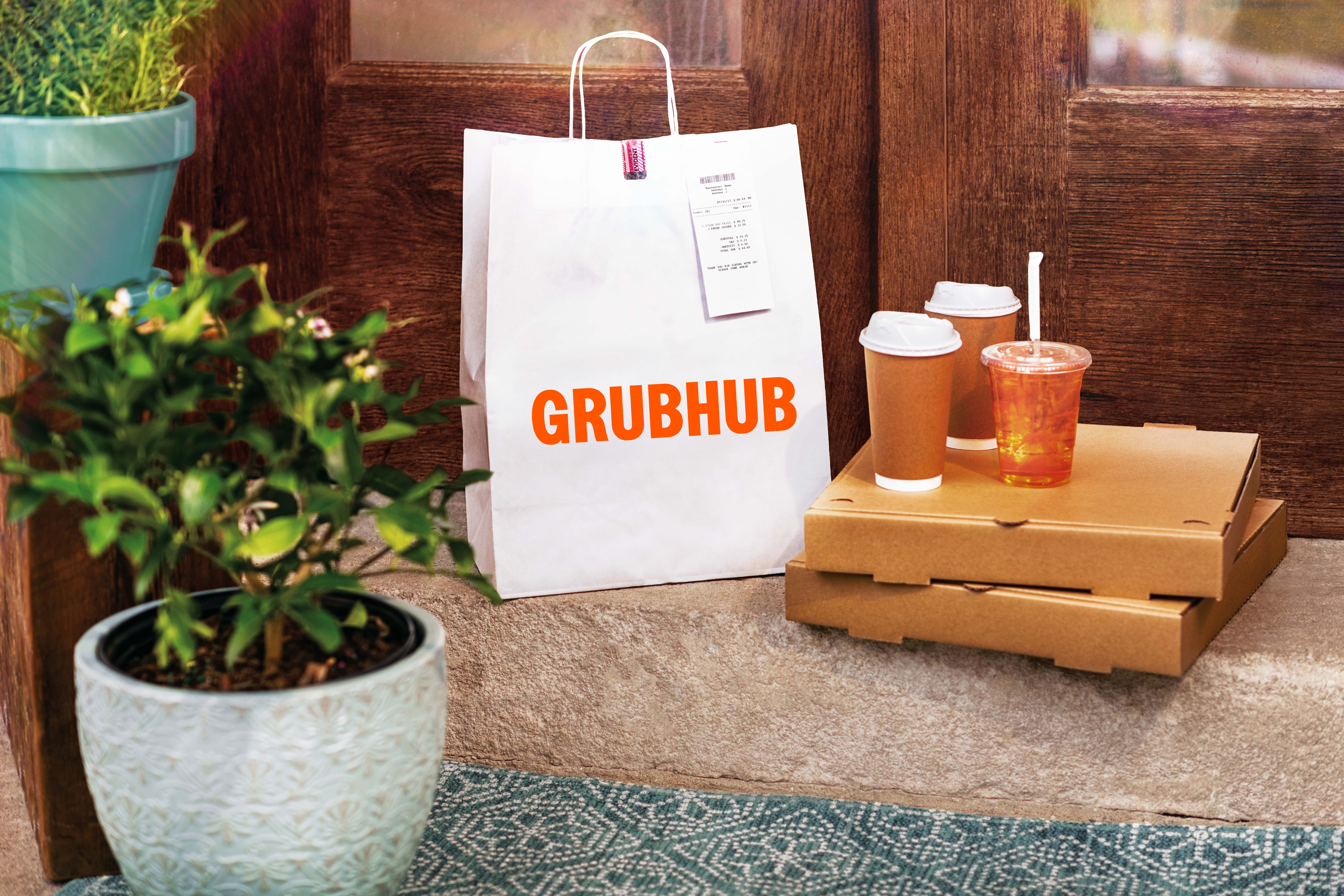 Grubhub bag sitting on doorstep next to two pizza boxes with two coffee cups and a tea on top of them.